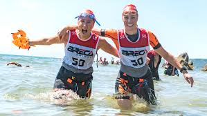 Two swimrun competitiors wearing red and white tops coming out of the sea