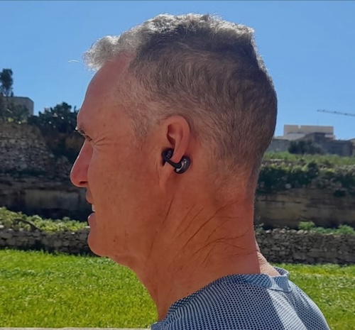 A man wearing Nank bluetooth ear buds, viewed from the side