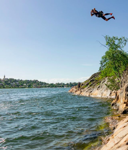 A man in a wetsuit jumping 20 meters into a lake at the EX swimrun event Falcon Mountain Base jump