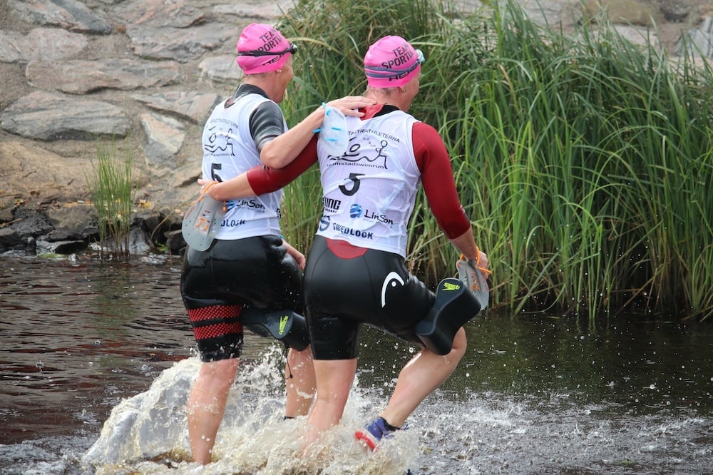 Two female swimrunners wading out of the water at the Halmstad swimrun, wearing pink hats Two female swimrunners wading out of the water at the Halmstad swimrun, wearing pink hats