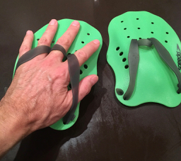 Two green SwimRun Paddles lying on a black surface, with a man's hand in the straps of the left one.