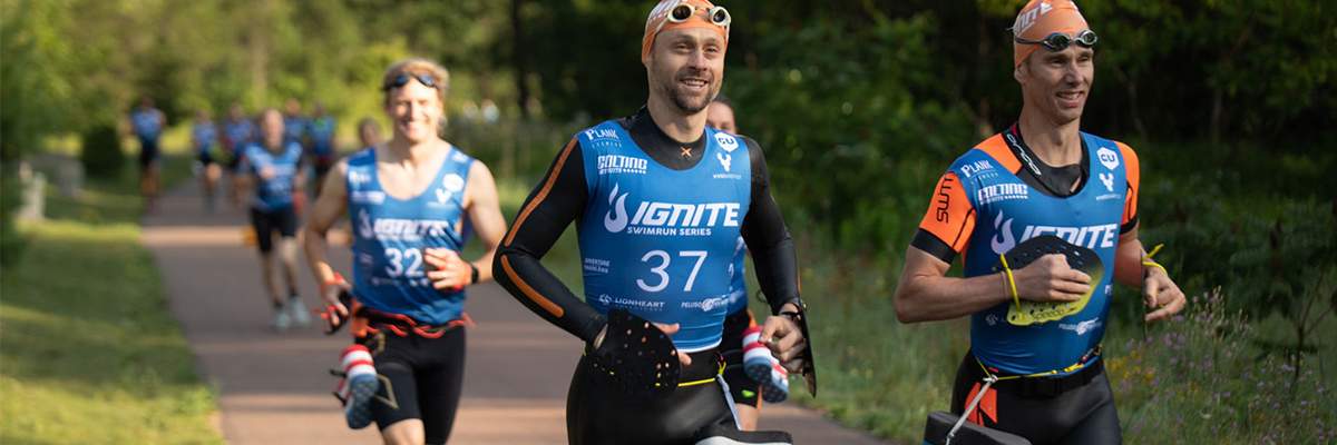 Two men and a woman in the background wearing blues running tops during a swimrun event. Two men and a woman in the background wearing blues running tops during a swimrun event.