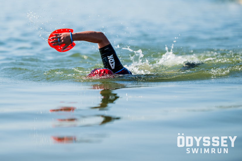 A man swimming with a red hand paddle in the Odyssey Swimrun at Austin, Texas. A man swimming with a red hand paddle in the Odyssey Swimrun at Austin, Texas.