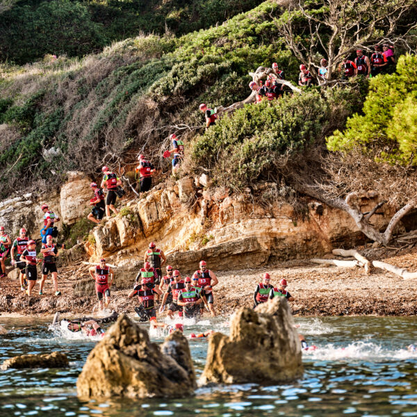 The Otillo Cannes swimrun race sea Entry, with swimrunners in red hats running into the sea in front of a cliff.