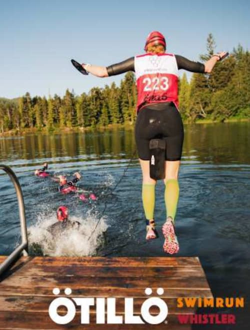 A man in a wetsuit and red hat jumping into a lake at the Otillo swimrun Whistler race