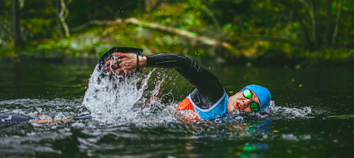 A woman swimrunner swimming with goggles, wetsuit and a blue swimcap in a river