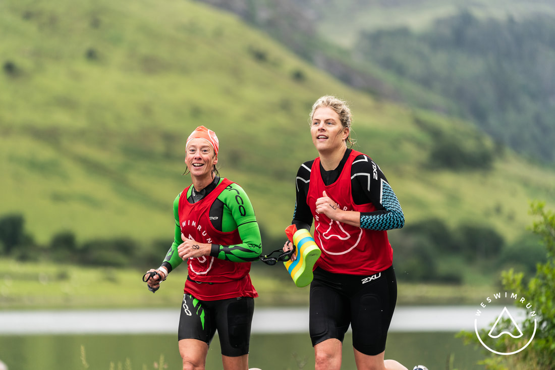 Tal Y Llyn swim exit with two female athletes in wetsuits and red race bibs Tal Y Llyn swim exit with two female athletes in wetsuits and red race bibs