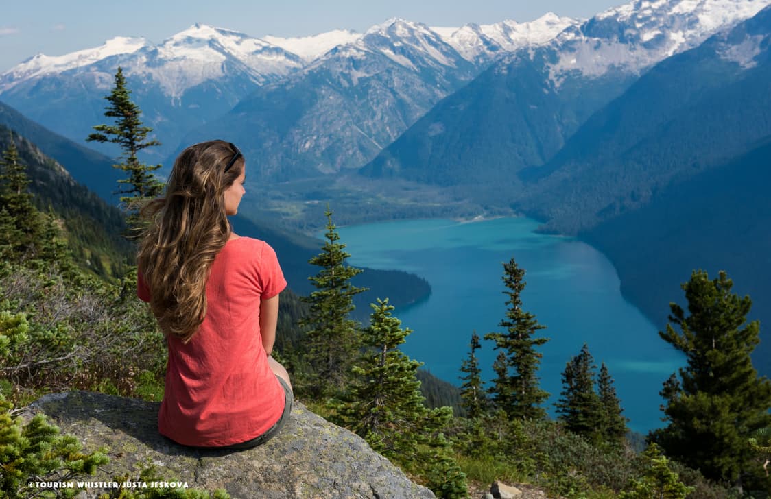 A young lady in a red top looks out over a mountain lake scene in Whistler, Canada