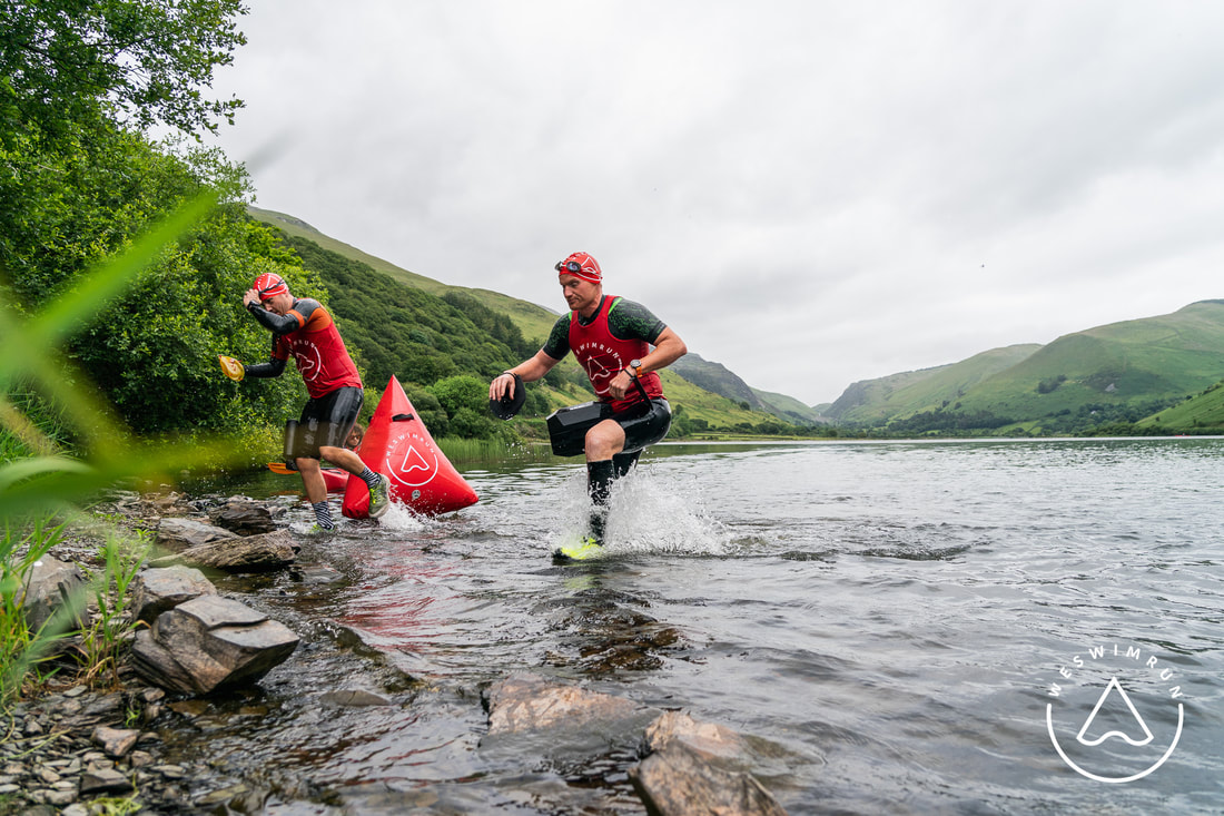 Two men in wetsuits and red tops clambering out of a welsh lake during Transition Training for Swimrun Two men in wetsuits and red tops clambering out of a welsh lake during Transition Training for Swimrun