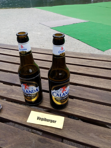 Two bottles of beer standing on a wooden table in a beer garden.