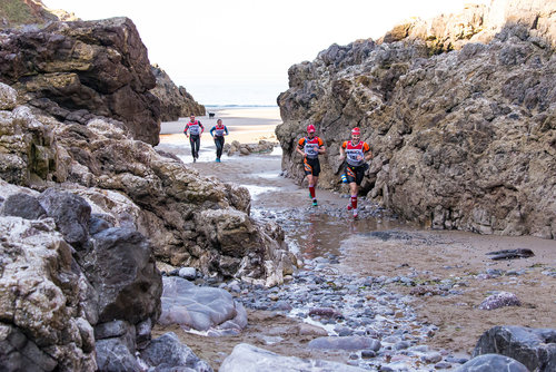 Swimrunners running on a sandy beach between rocky outcrops
