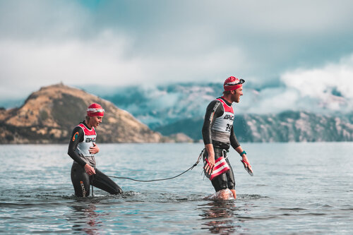 Two swimrunners  walking out of Lake Wanaka in New Zealand, with mountains in the background.