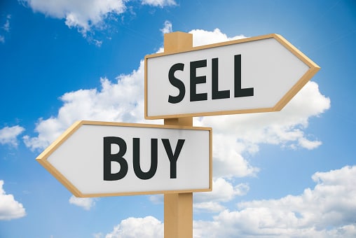 A buy and sell sign with a blue sky and some white clouds in the background.
