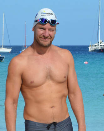 A swimmer wearing hat and goggles standing in a beach with blue sea in the background