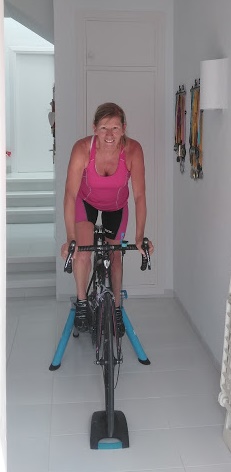 A woman in a pink top on an indoor bike, exercising.