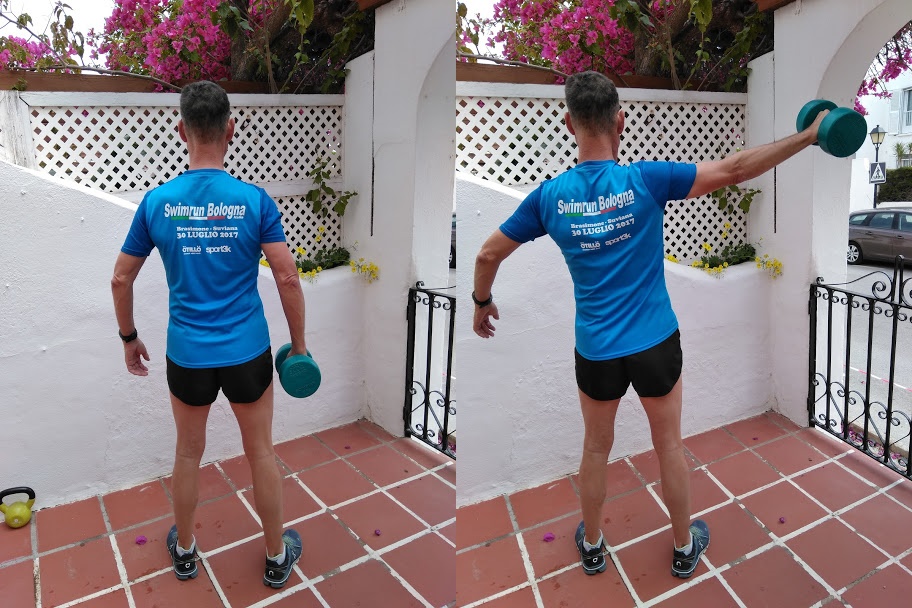 A man wearing a blue top, demonstrating a lateral arm raise with a dumbell.