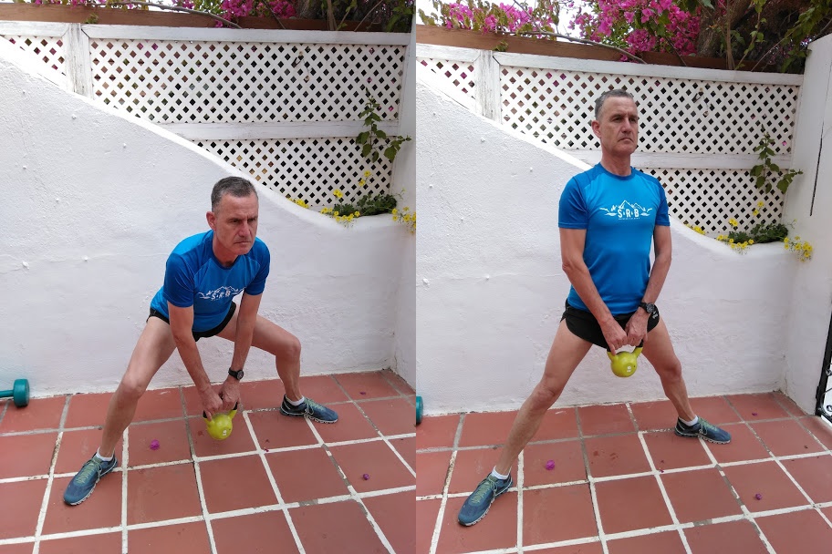 A man in a blue top demonstrating a sumo squat with a kettle bell weight