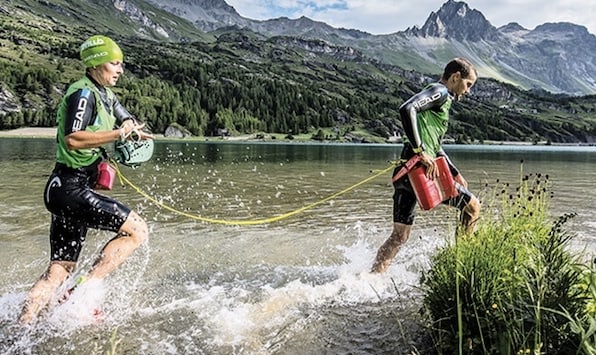 Two swimrun competitors leaving the water, joined by a tether Two swimrun competitors leaving the water, joined by a tether