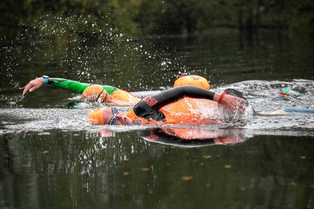 Two people in wetsuits and colored tops swimming in a lake at a Gritty Rascals swimrun event Two people in wetsuits and colored tops swimming in a lake at a Gritty Rascals swimrun event