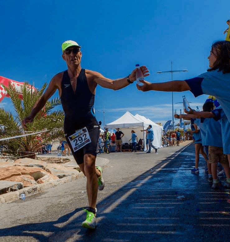 A triathlete in a black top and yellow cap grabbing a water bottle at Torrevieja Triathlon