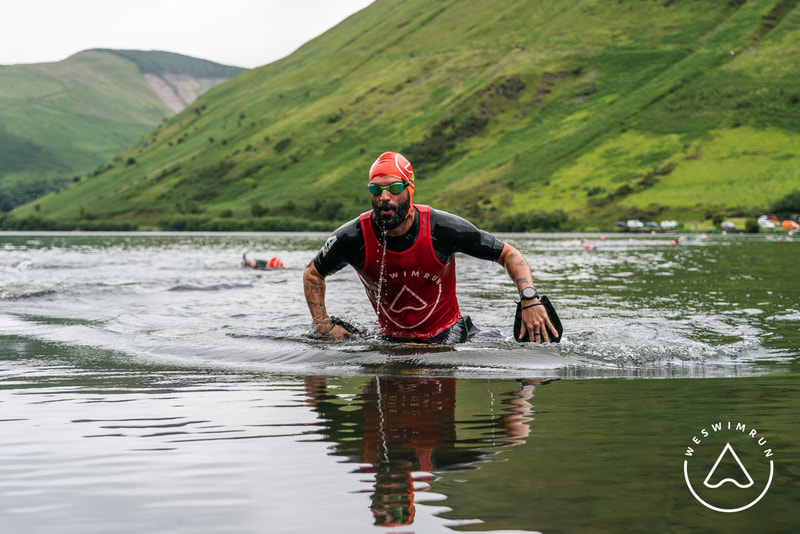 A man in a wetsuit and red top with swim goggles walking out of the water at the Swimrun Dyfi swimrun event A man in a wetsuit and red top with swim goggles walking out of the water at the Swimrun Dyfi swimrun event