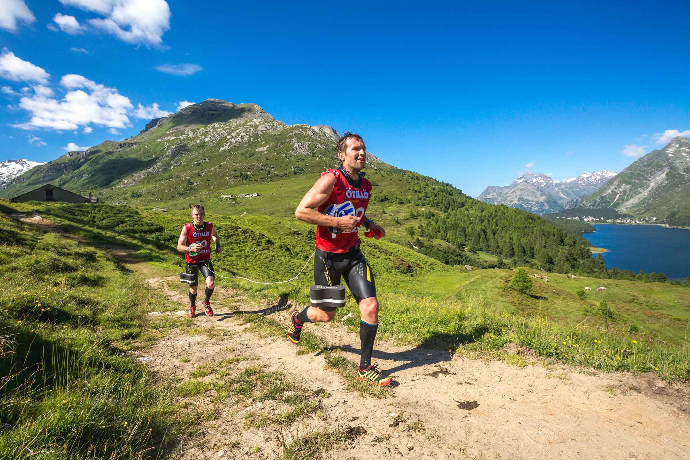 Two swimrun competitors running a mountain trail on a sunny day