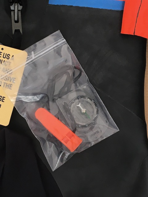 a compass and an orange whistle in a clear plastic bag.
